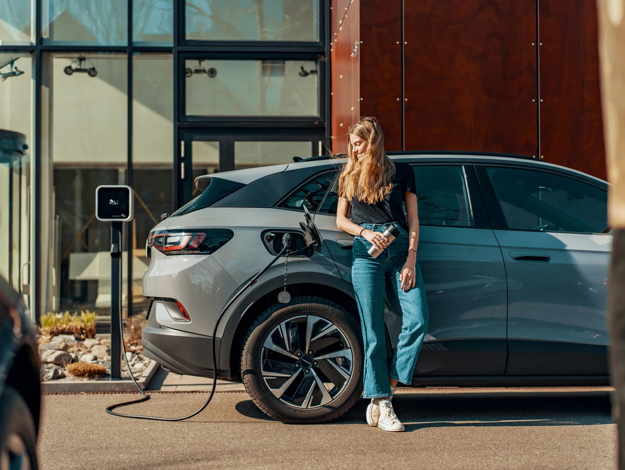 Pessoa encostada a um SUV eléctrico a carregar num posto